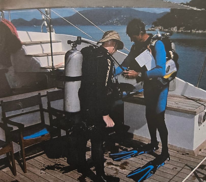 Jimmy gearing up a scuba diver on a dive boat overlooking the bay