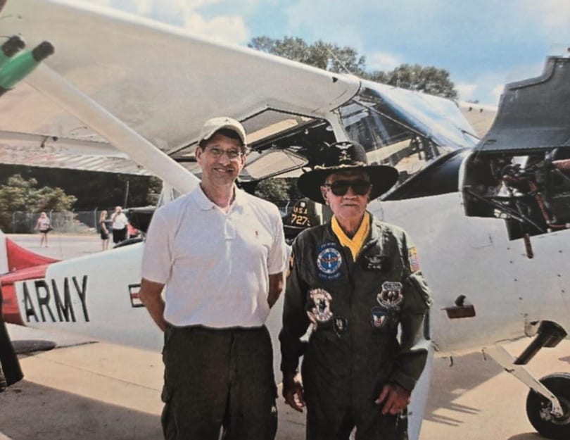 Jimmy in a flight jacket beside a vintage Army airplane at an airshow