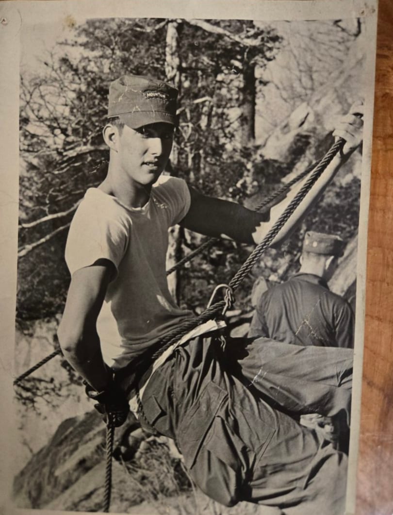 Young man in a "MOUNTAIN" cap and t-shirt, holding ropes while rappelling down a rocky incline.
